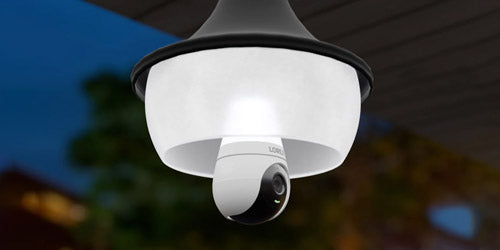 Lorex 2K Wi-Fi lightbulb security camera mounted in an outdoor ceiling fixture at dusk, with its status light glowing and surroundings softly lit.